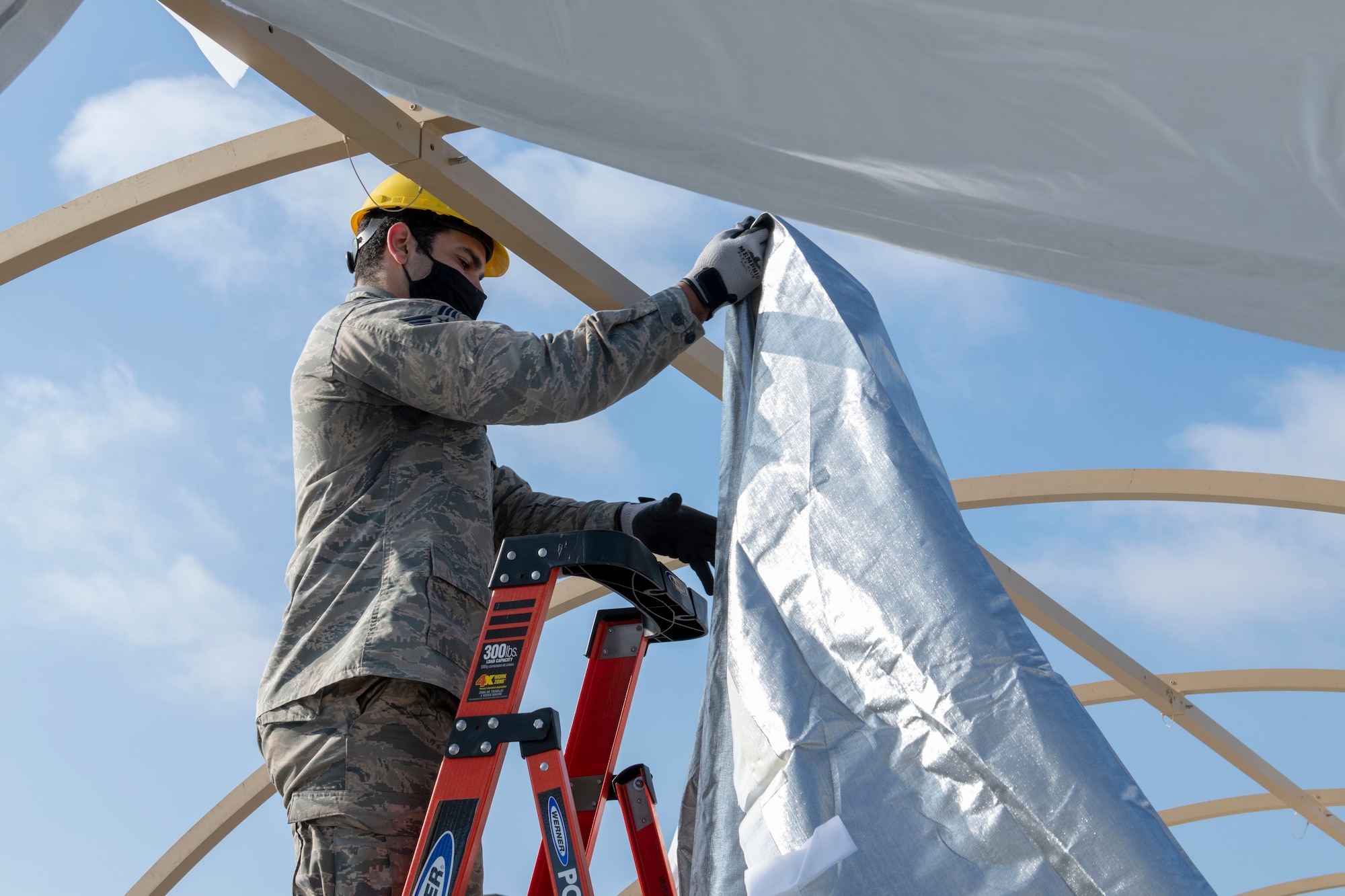 Man stands on ladder draping outer layer of tent over frame