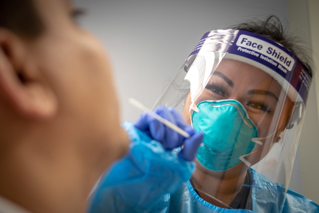 A nurse wearing a facemask and face shield does a nasal swab test.