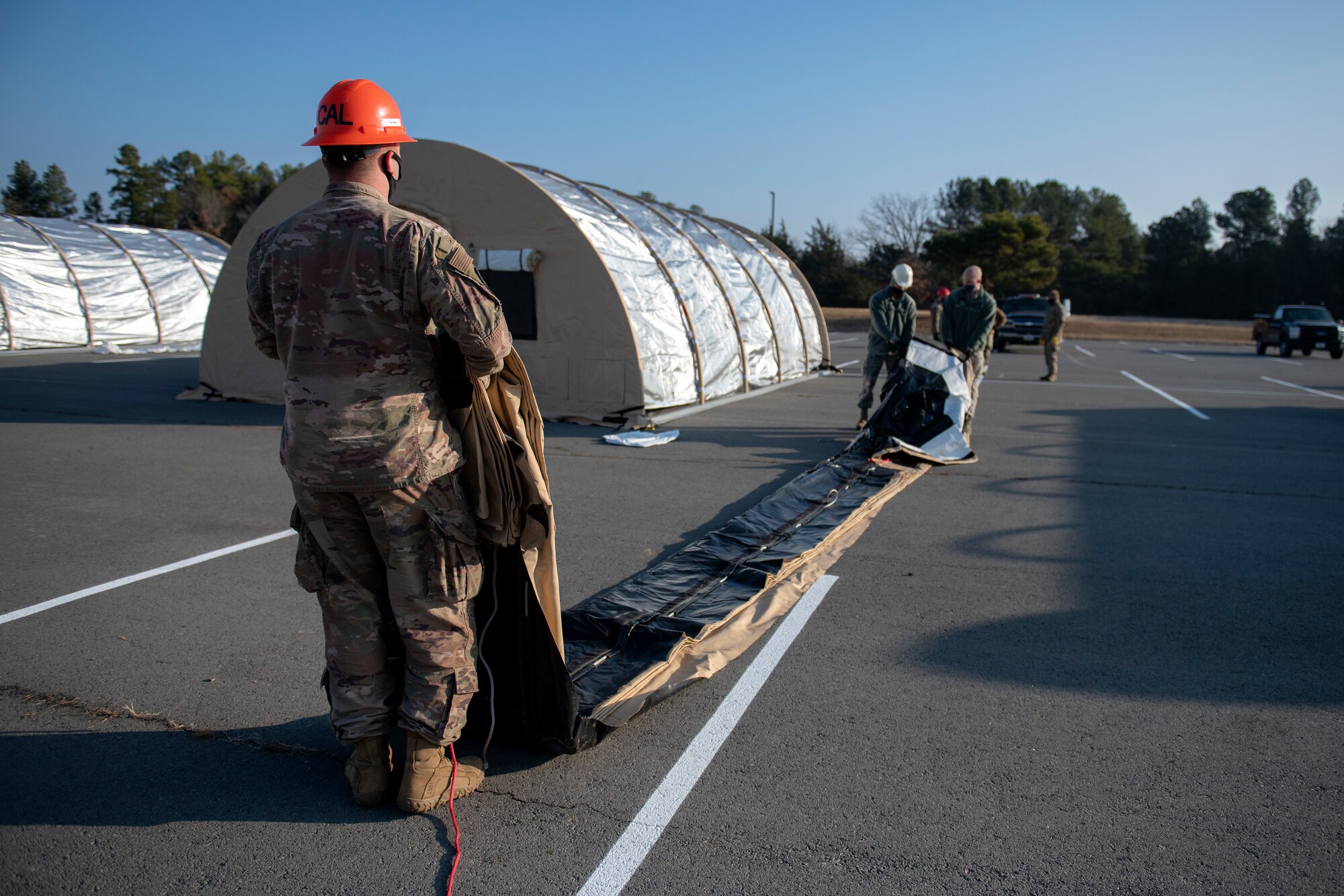 Man lays out large outer cover of tent on ground