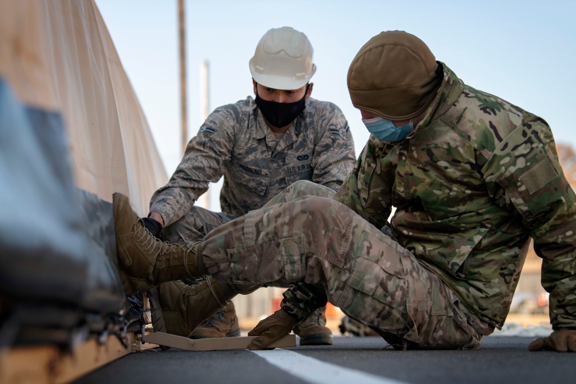 two men strect rope along the bottom of the tent to secure it to the frame