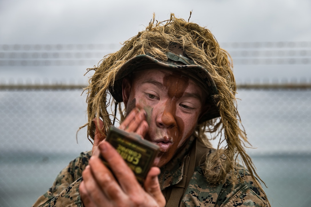 A Marine covers his face with brown camouflage paint.