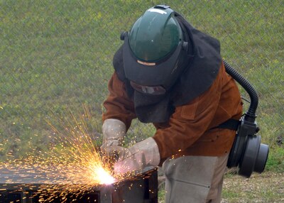 A person uses a cutting torch on scrap metal and sparks fly.