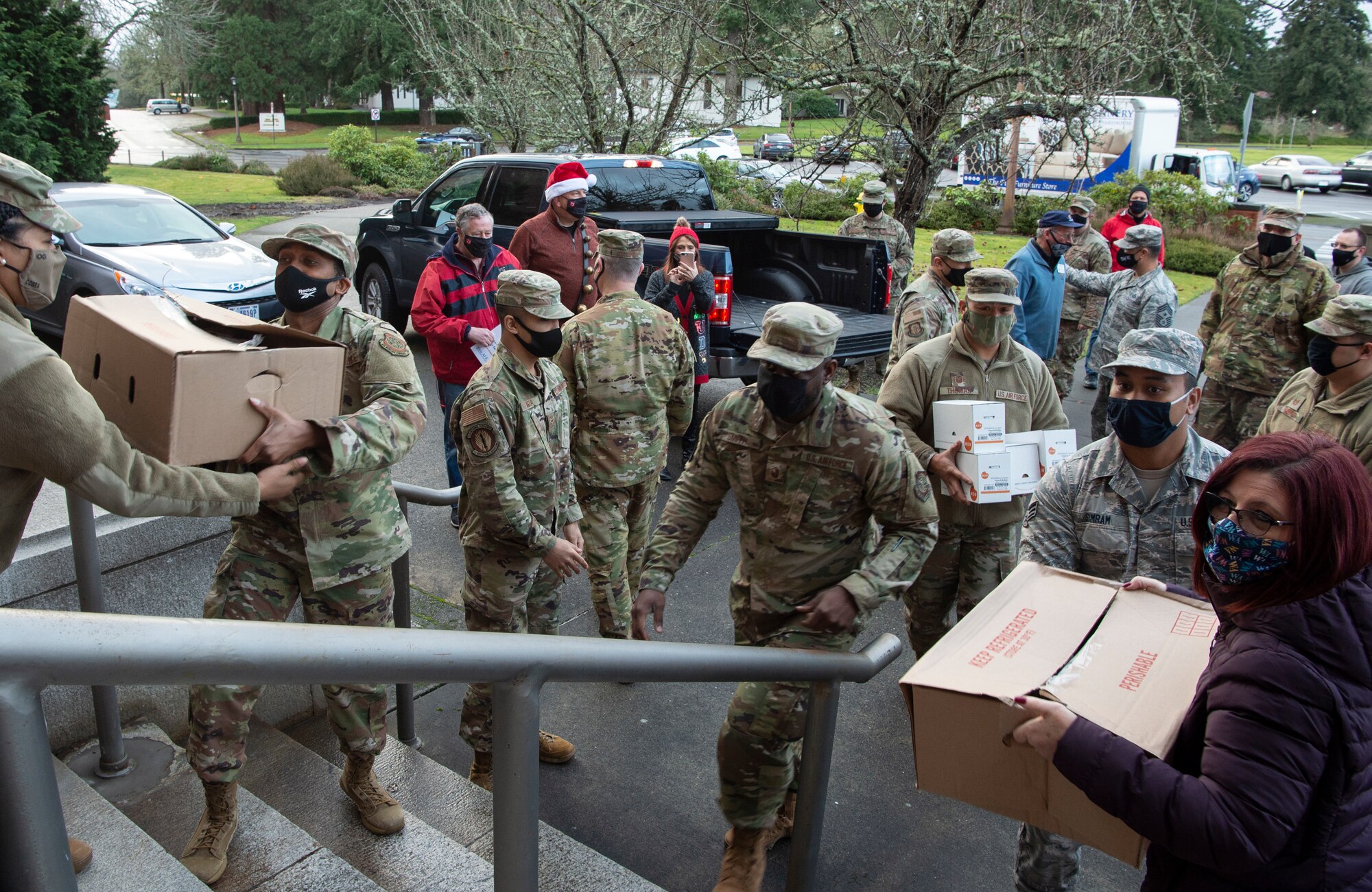 Airmen and civilians assigned to the 62nd Airlift Wing pass boxes of hams to the front of the wing headquarters building during Operation Ham Grenade at Joint Base Lewis-McChord, Wash., Dec. 17, 2020. The purpose of ham grenade is to provide hams for Airmen and their families during the holidays. (U.S. Air Force photo by Senior Airman Tryphena Mayhugh)