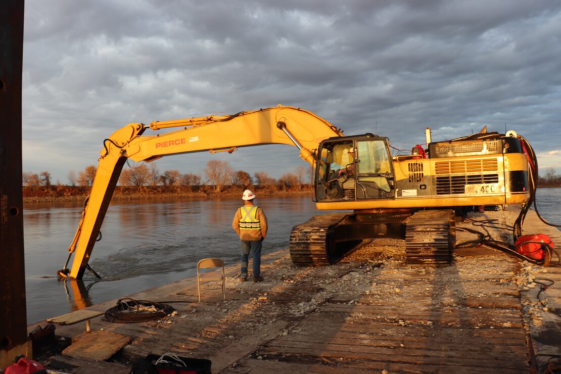 A Kansas City District track-hoe on a barge work boat took part in hydrodynamic dredging operations on the Missouri River November 11, 2020. The hydrodynamic dredge head is mounted on the bucket and the arm directs the flow the desired area of concern to be affected. The Engineering Research and Development Center brought the system to Kansas City District from Vicksburg, Miss., to assist in clearing shoals that developed on the Missouri River due to damages from flooding to the river control structures. The device enabled the combined team to redirect sandy material back into suspension in the current of the river and away from the built-up areas that impede navigation on the river.