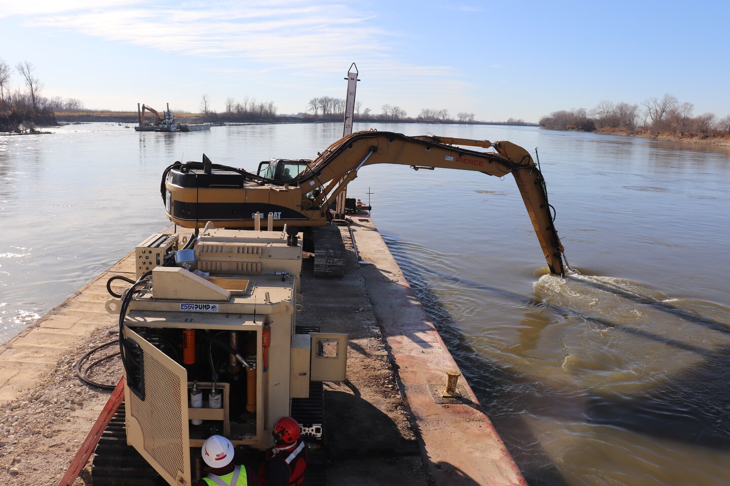 A Kansas City District track-hoe on a barge work boat took part in hydrodynamic dredging operations on the Missouri River November 11, 2020. The hydrodynamic dredge head is mounted on the bucket and the arm directs the flow the desired area of concern to be affected. The Engineering Research and Development Center brought the system to Kansas City District from Vicksburg, Miss., to assist in clearing shoals that developed on the Missouri River due to damages from flooding to the river control structures. The device enabled the combined team to redirect sandy material back into suspension in the current of the river and away from the built-up areas that impede navigation on the river.