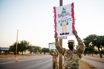 U.S. Air Force Master Sgt. Quintin Bradley (right), and Tech. Sgt. Cassandra Elchelberger, both with the Air Force Services Center, hold signs to spread holiday cheer for drivers to see Dec. 18, 2020, at Joint Base San Antonio-Lackland, Texas.