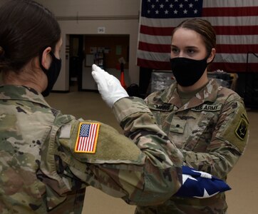 Cadet Haley Kieny, left, salutes Cadet Hannah Minns after presenting her a folded American flag during military funeral honors practice at Camp Johnson, Vermont, Dec. 18, 2020. The 40-hour Honor Guard course trains Soldiers how to conduct color guards, funeral honors and other ceremonies. The cadets are assigned to the University of Vermont-Montpelier Army ROTC. (U.S. Army National Guard photo by Don Branum)