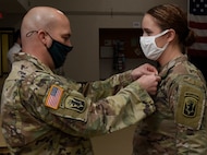 Maj. Jason Beams presents Cadet Hannah Minns with an Army Achievement Medal during a recognition ceremony at Camp Johnson, Vermont, Dec. 18, 2020. Minnis, a cadet with University of Vermont ROTC, received a perfect score in the Vermont Army National Guard’s Military Funeral Honors training, a 40-hour course that prepares Soldiers to render services for funerals, color guards, and other formal ceremonies. Beans is the Vermont National Guard liaison and operations officer for the UVM ROTC Program. (U.S. Army National Guard photo by Don Branum)