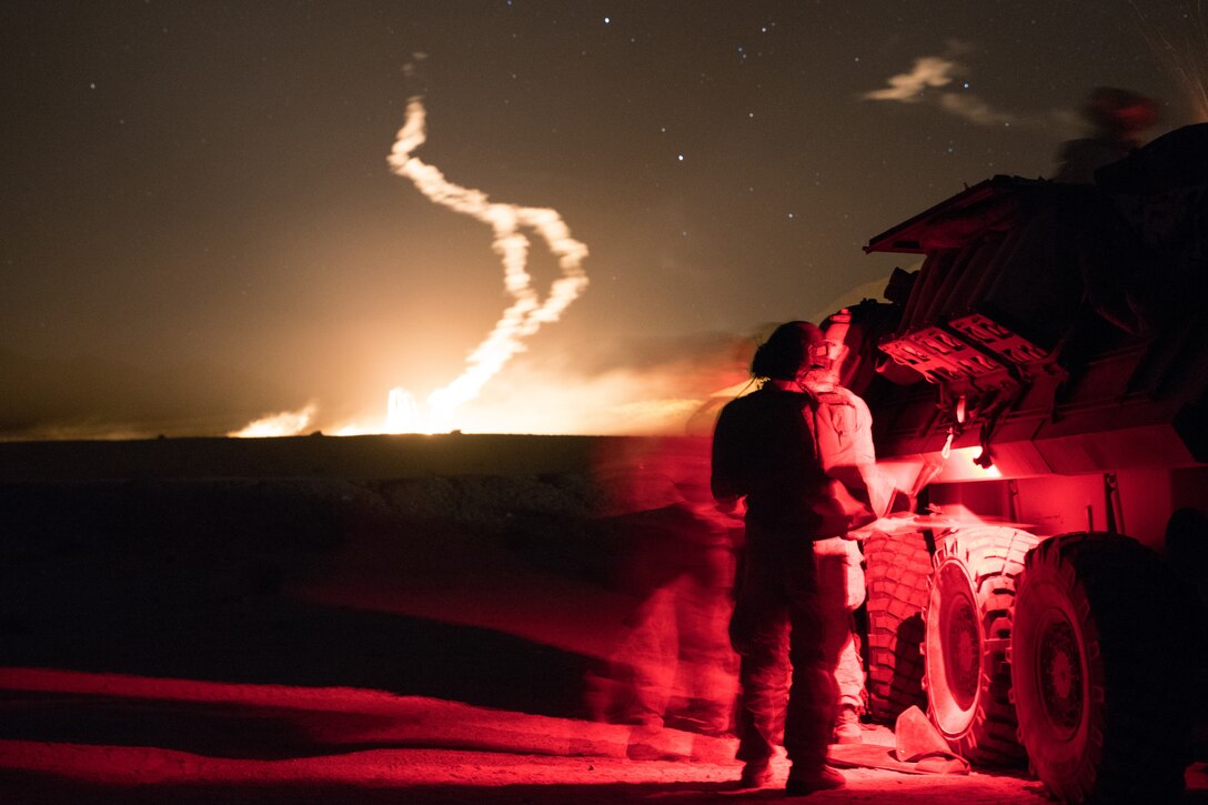 Marines stand together next to a vehicle in a red glow at night.