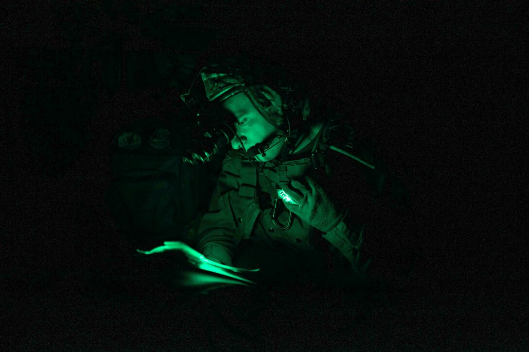 A Marine illuminated by green light uses a flashlight to look at a paper.