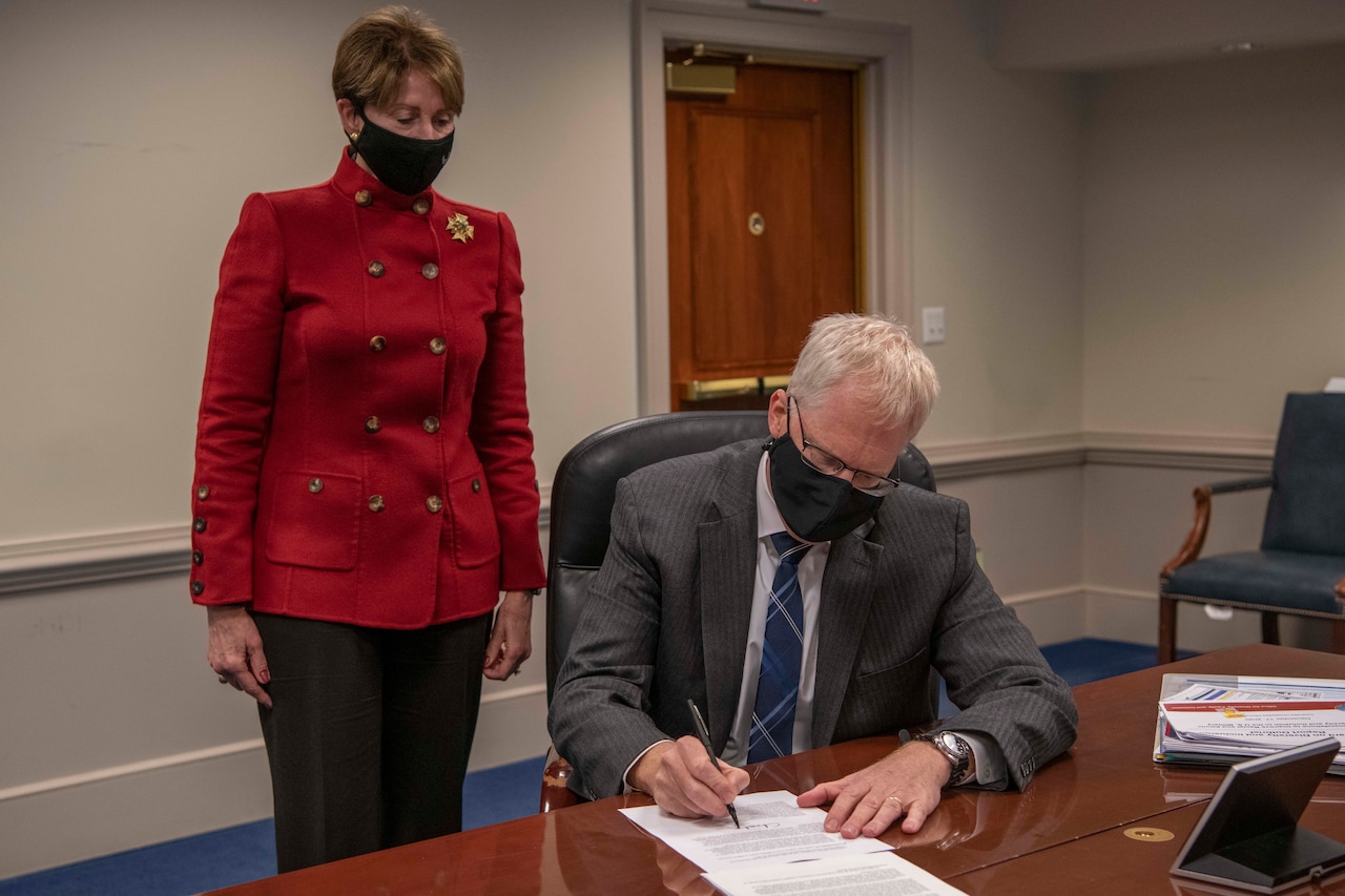 A man signs a document while a woman watches.