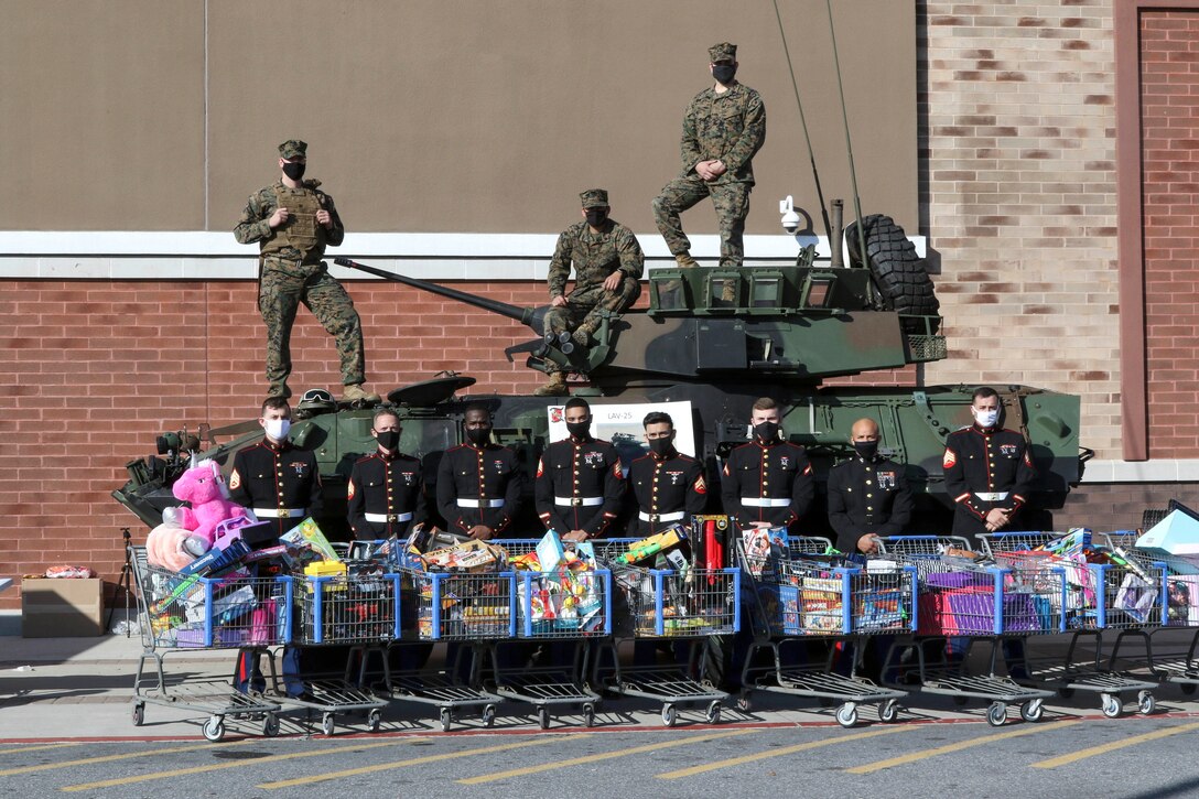 Marines stand for a photo in a parking lot with a tank and grocery carts filled with toys.