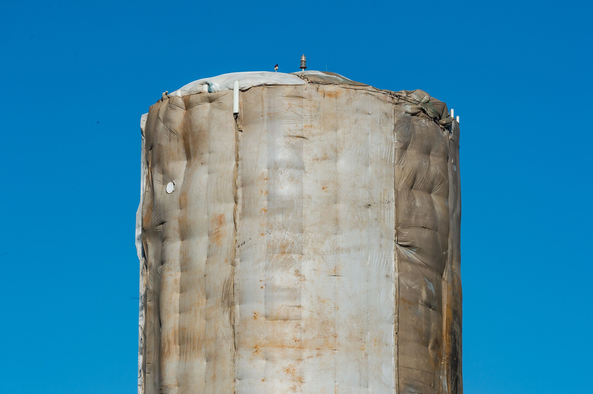 Protective sheathing surrounds scaffolding and the base water tower as employees from a contracted company continue periodic internal and external maintenance to the tower, Dec. 8, 2020, on Dover Air Force Base, Delaware. The water tower is operated by Tidewater Utilities, Inc. who subcontracted the blasting and painting of the tower. Site preparation and mobilization started in August, with a projected completion date at the end of December, weather permitting. (U.S. Air Force photo by Roland Balik)