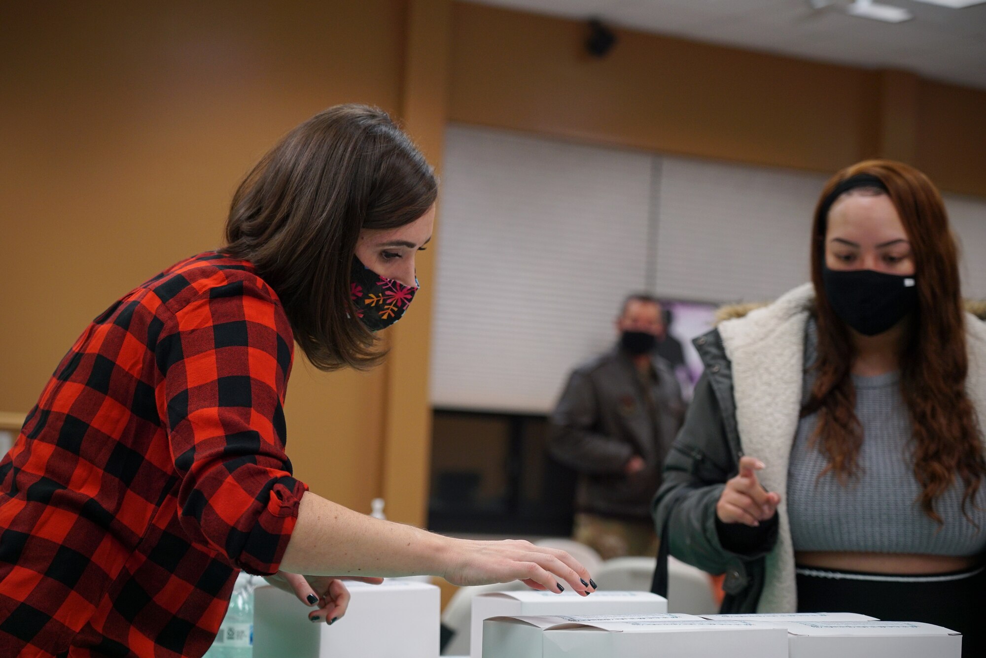 A woman in the left-hand frame leans over a row of white cardboard lunch boxes lined up on a table.