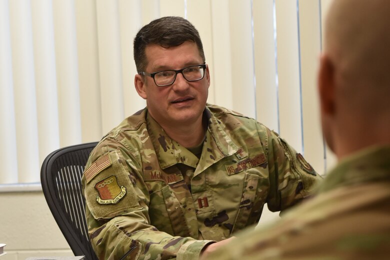 Photo shows man sitting behind desk speaking to another man.