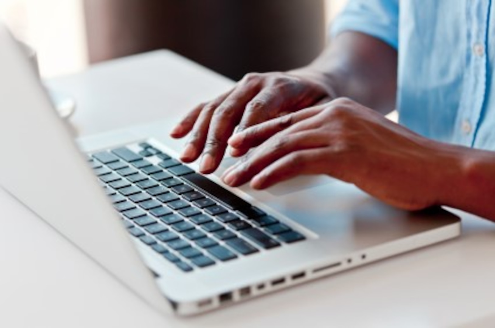 A photograph of hands typing on a silver laptop