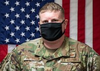 Photo of an Airmen standing in front of a flag background