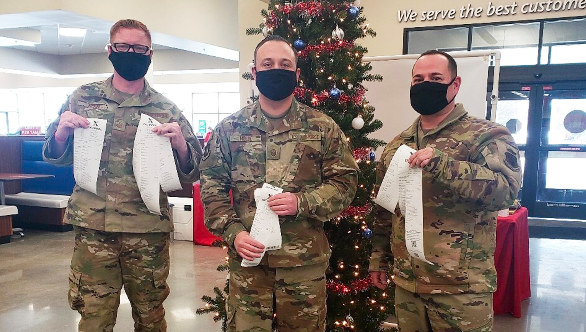 Three first sergeants stand in front of a Christmas tree holding up receipts they received from paying off layaways.