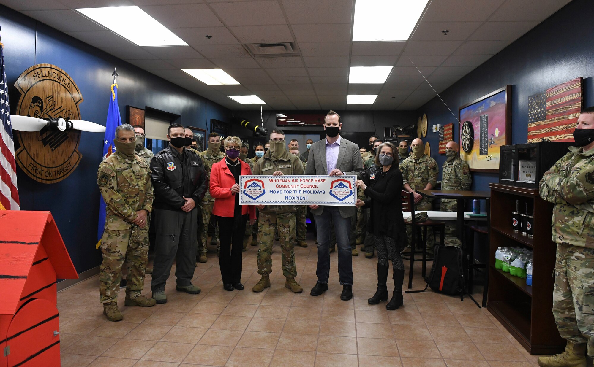 A group of Airmen stand inside the breakroom of the 20th Attack Squadron with a "Home for the Holidays" selectee.