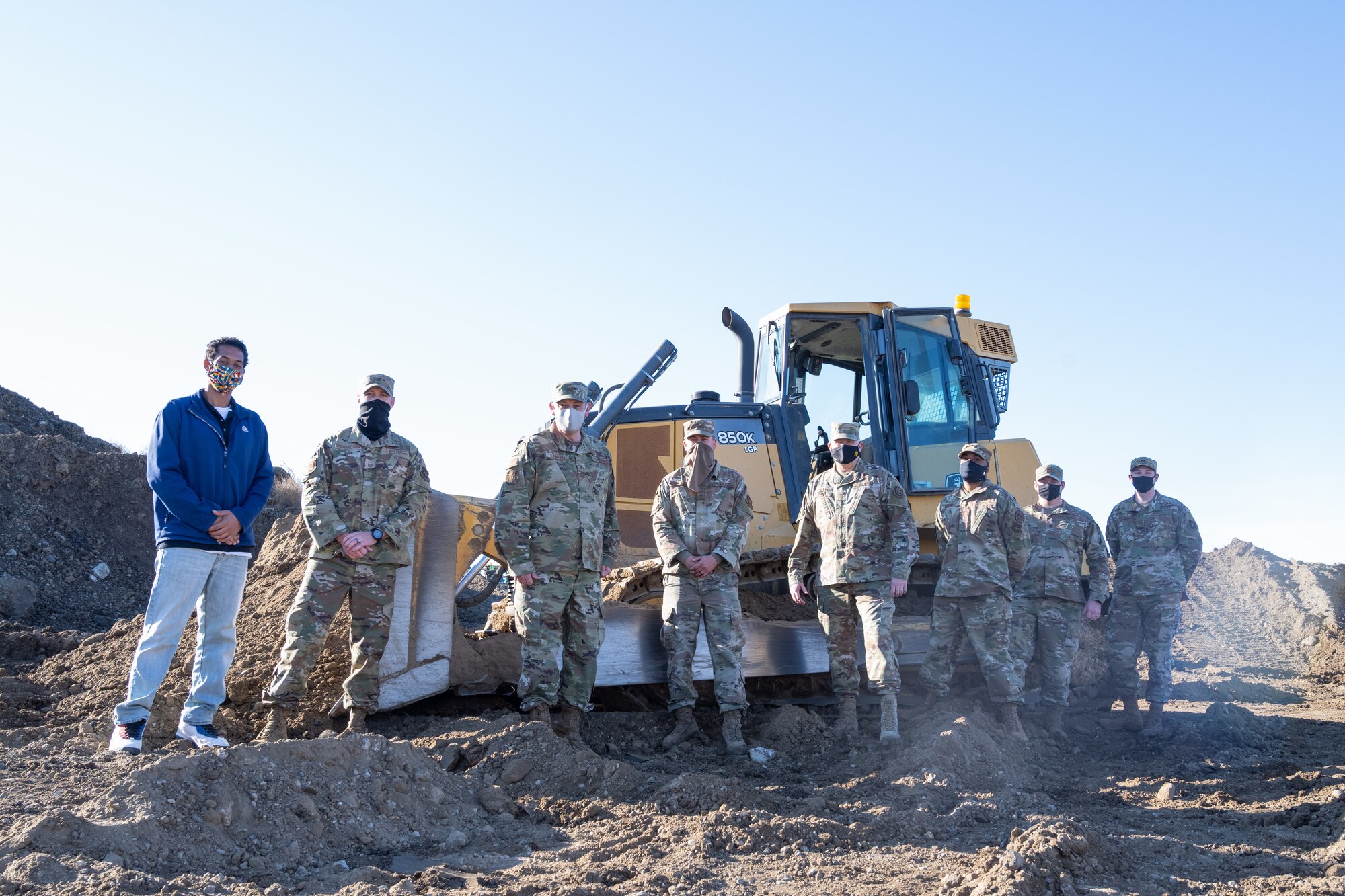 Airmen pose for camera in front of a bulldozer.