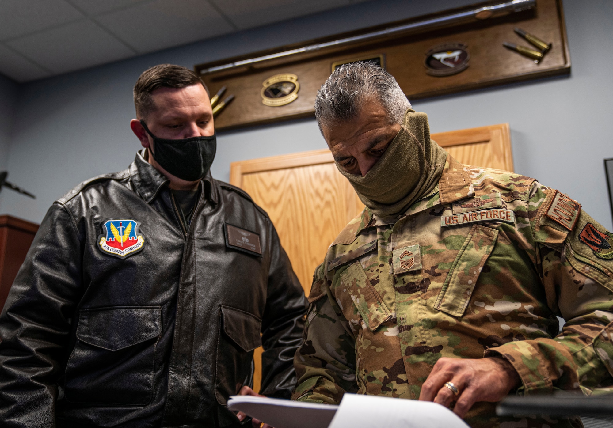 Two Airmen stand next to each other and view paperwork regarding the "Home for the Holidays" program.