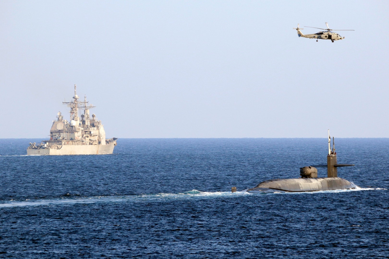The guided-missile submarine USS Georgia (SSGN 729), right, transits the Strait of Hormuz with the guided-missile cruiser USS Port Royal (CG 73), the guided-missile cruiser USS Philippine Sea (CG 58), not pictured, and a MH-60R Sea Hawk helicopter, attached to Helicopter Maritime Strike Squadron (HSM) 48, Dec. 21. Georgia is deployed to the U.S. 5th Fleet area of operations in support of naval operations to ensure maritime stability and security in the Central Region, connecting the Mediterranean and Pacific through the Western Indian Ocean and three critical chokepoints to the free flow of global commerce.