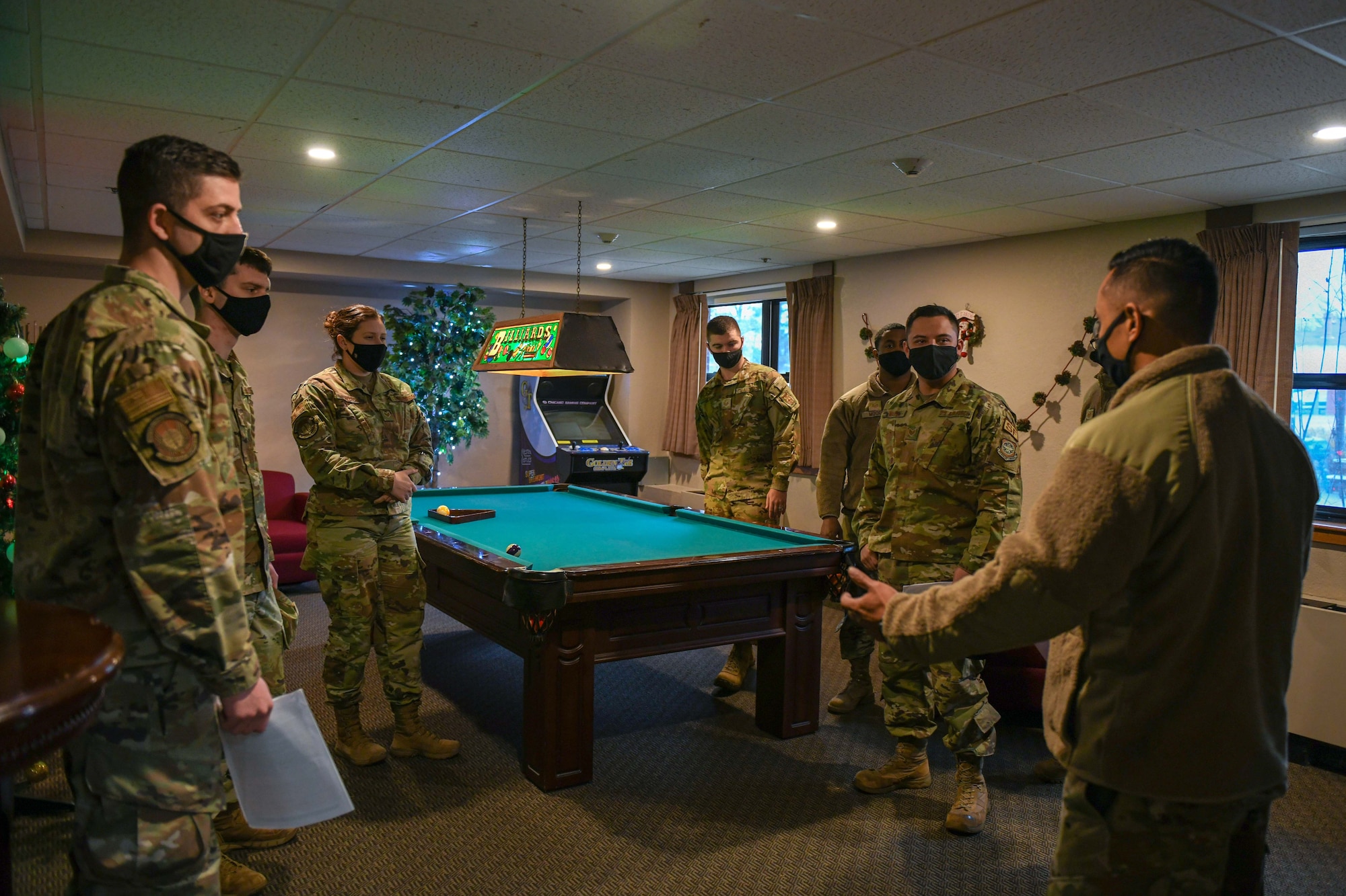 Airmen stand around a pool table discussing an ALS course.