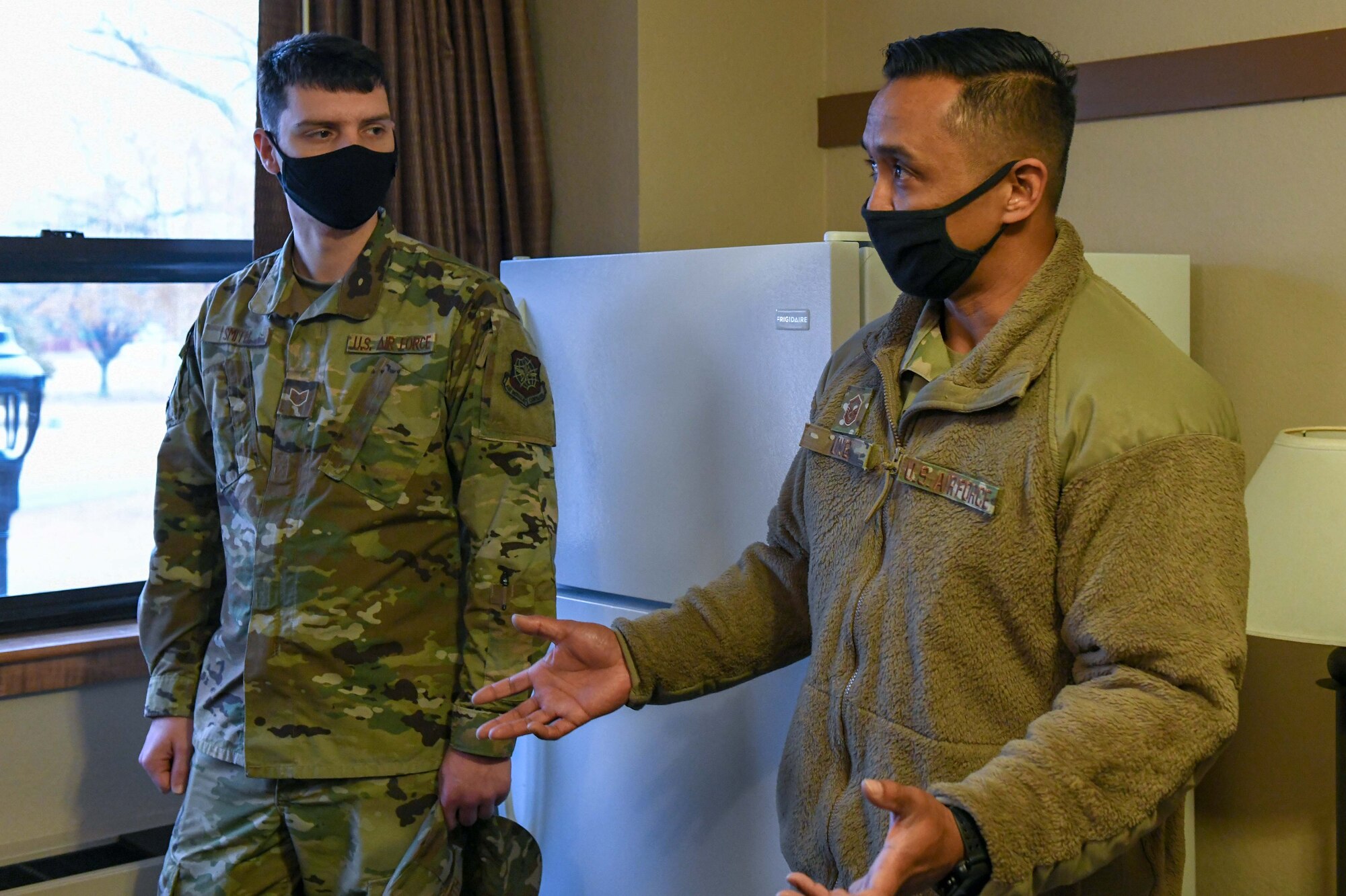 Airmen stand around a dorm room, showcasing what to look for during an inspection.