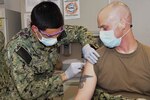 Hospitalman Roman Silvestri administers one of the first COVID-19  vaccines given at Naval Medical Center Portsmouth (NMCP) to Cmdr. Joseph Kotora, Medical Services director, and Emergency Medical Services Medical Director for Naval Medical Forces Atlantic, Dec. 15.