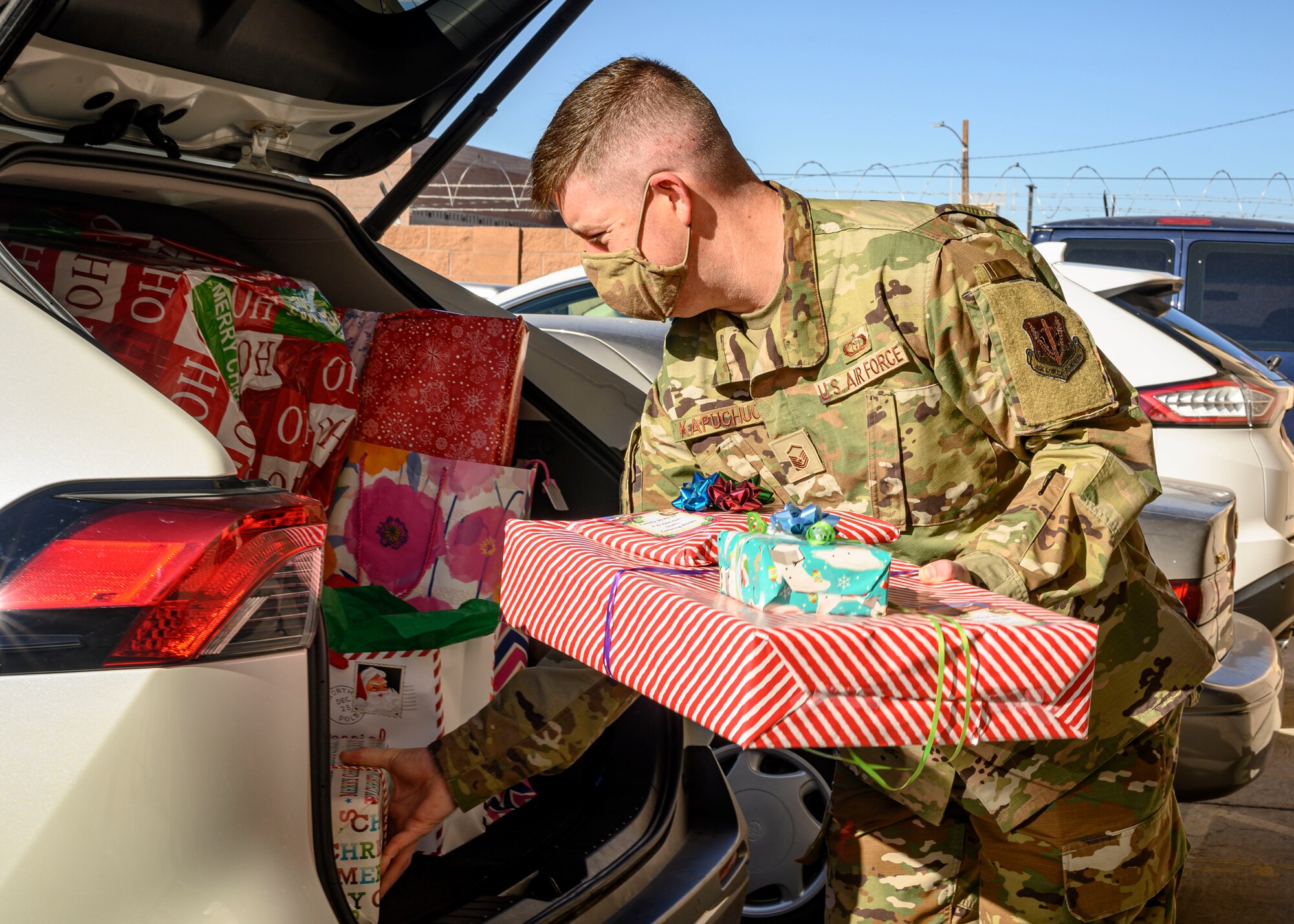 A first sergeant loads wrapped presents into a car