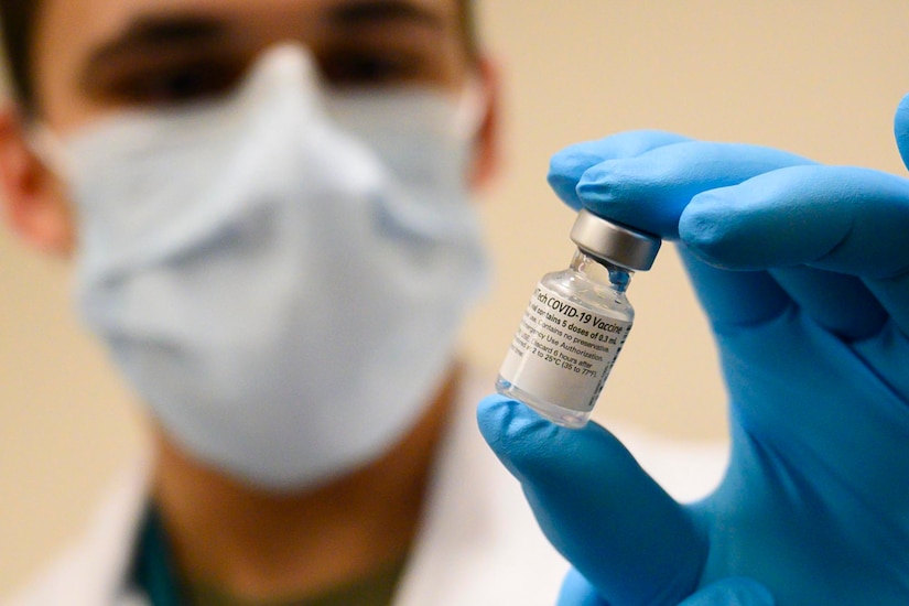 A soldier holds a vial between his fingers.