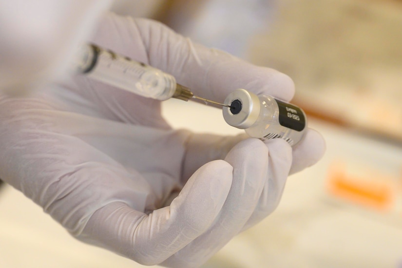 A sailor’s gloved hand extracting liquid from a vial.