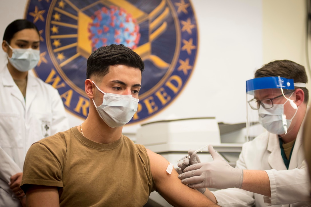 A sailor gets a shot in the arm from medical personnel.