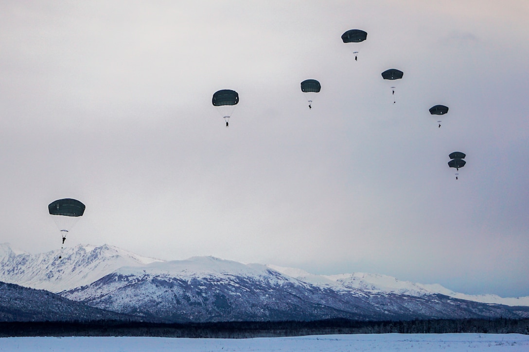 Soldiers freefall while wearing parachutes with snowy mountains in the background.