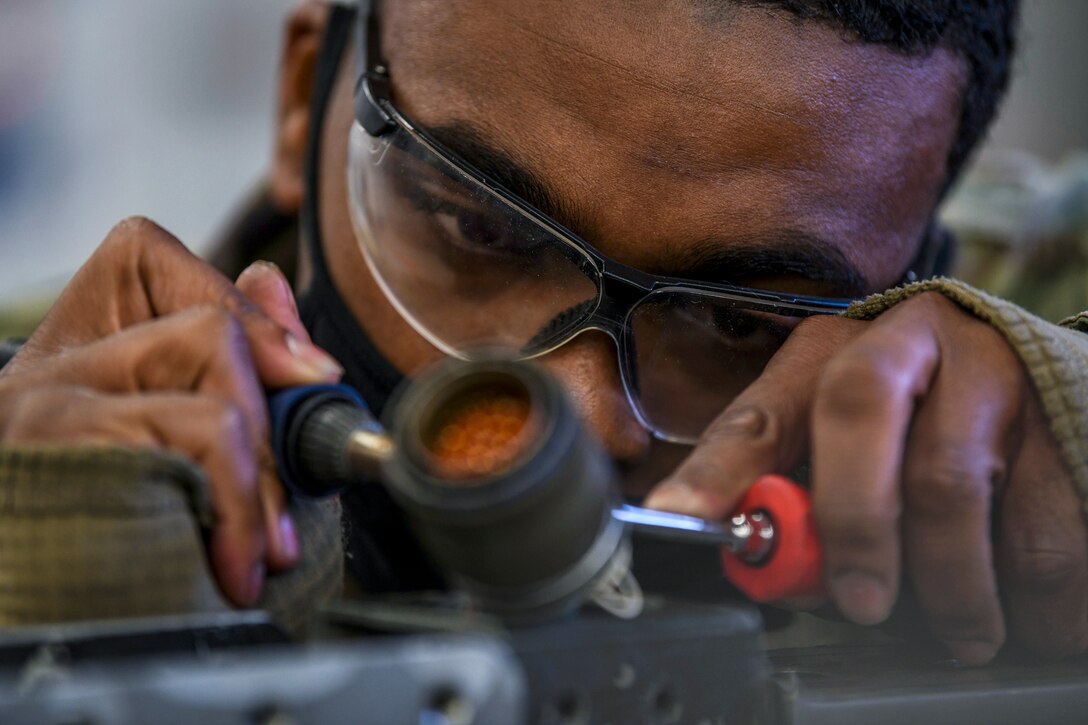 An airman wearing protective eyewear uses tools on rail equipment.