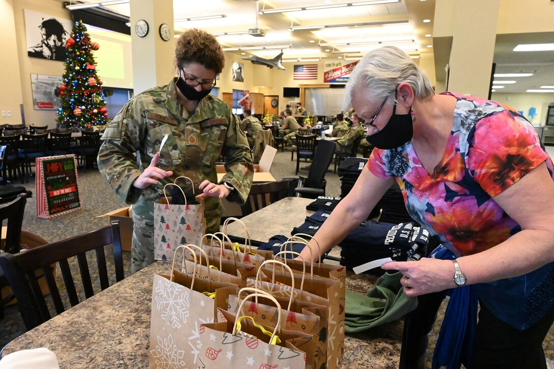 A military member in uniform, left, and a civilian employee package Christmas gifts to deliver to residents of the North Dakota Veterans Home, Lisbon, N.D. at the North Dakota Air National Guard Base, Fargo, N.D., Dec. 16, 2020.