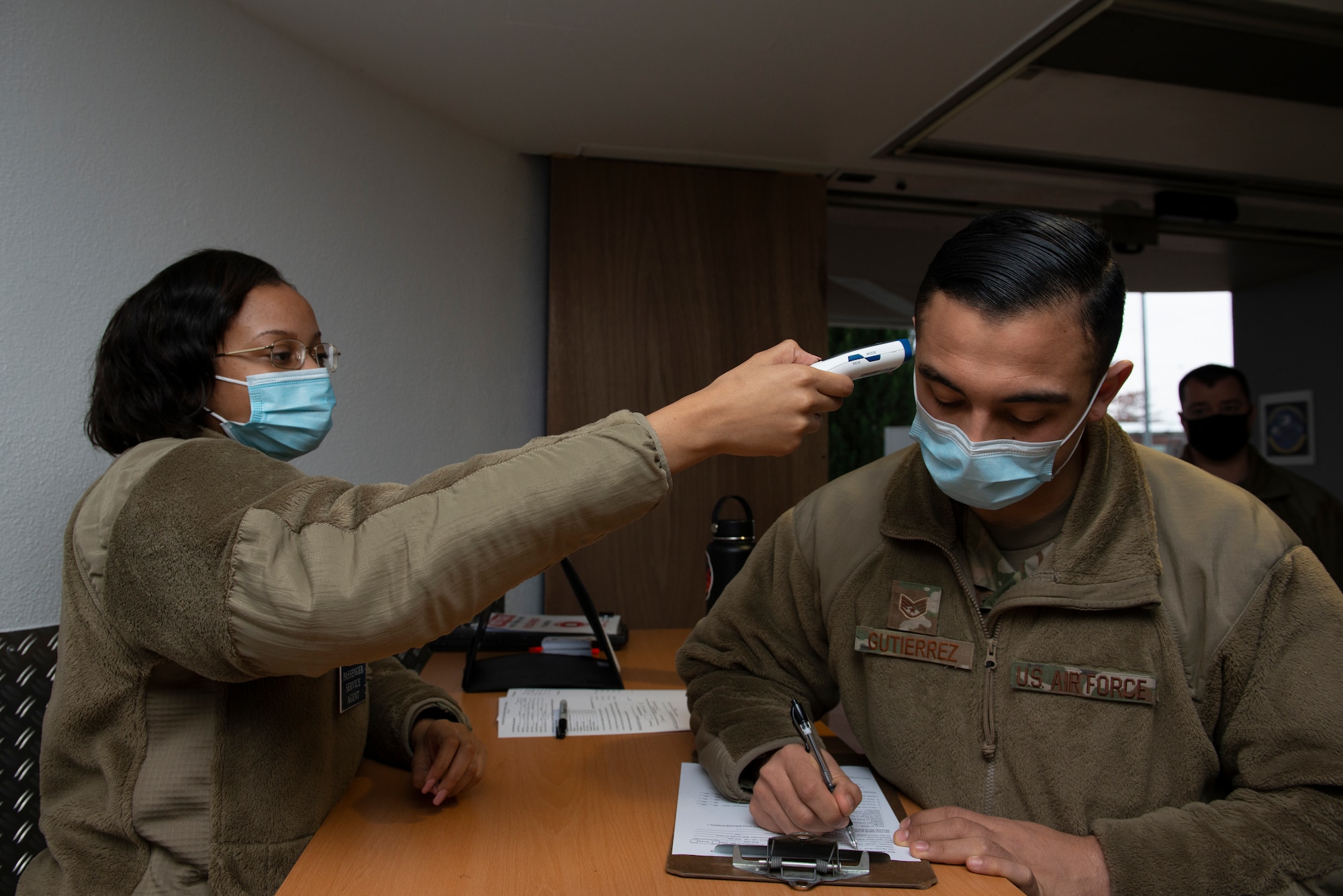 A photo of an Airman checking another Airman's temperature.