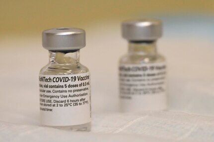 Two vials of COVID-19 vaccine sit on a white surface.