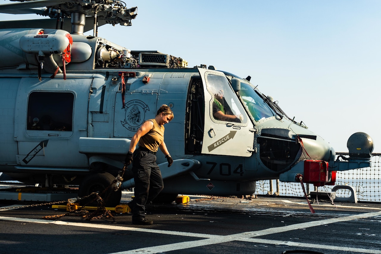 A woman drags a chain behind her as she walks beside a helicopter.