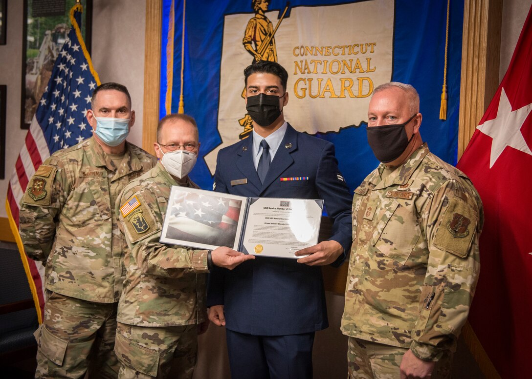 Four men in masks stand in front of a Connecticut Air National Guard flag. The middle two hold an award certificate.