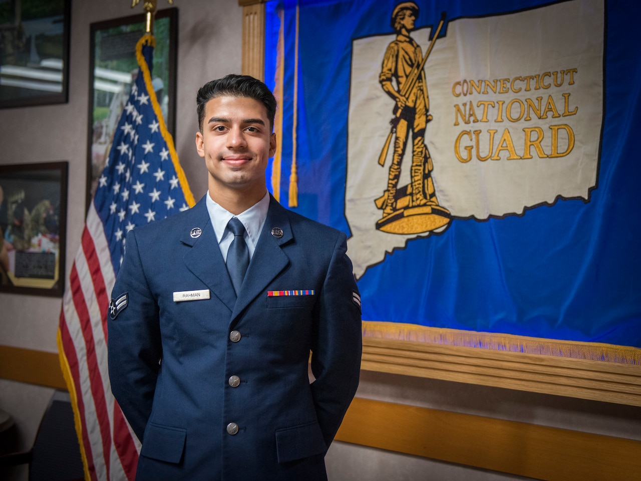An airman stands in front of a Connecticut Air National Guard flag.