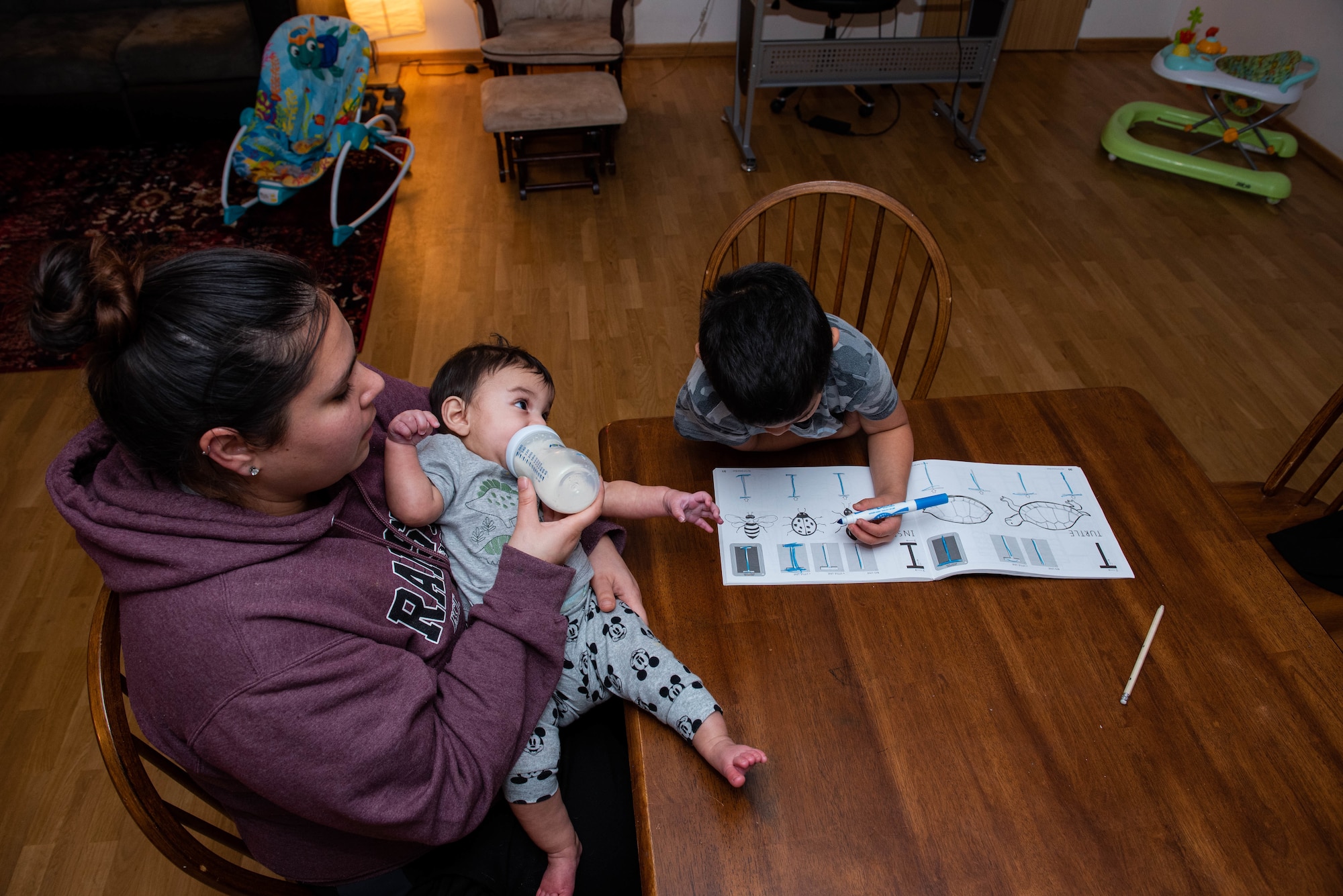 Photo of boy doing homework while mom feeds baby