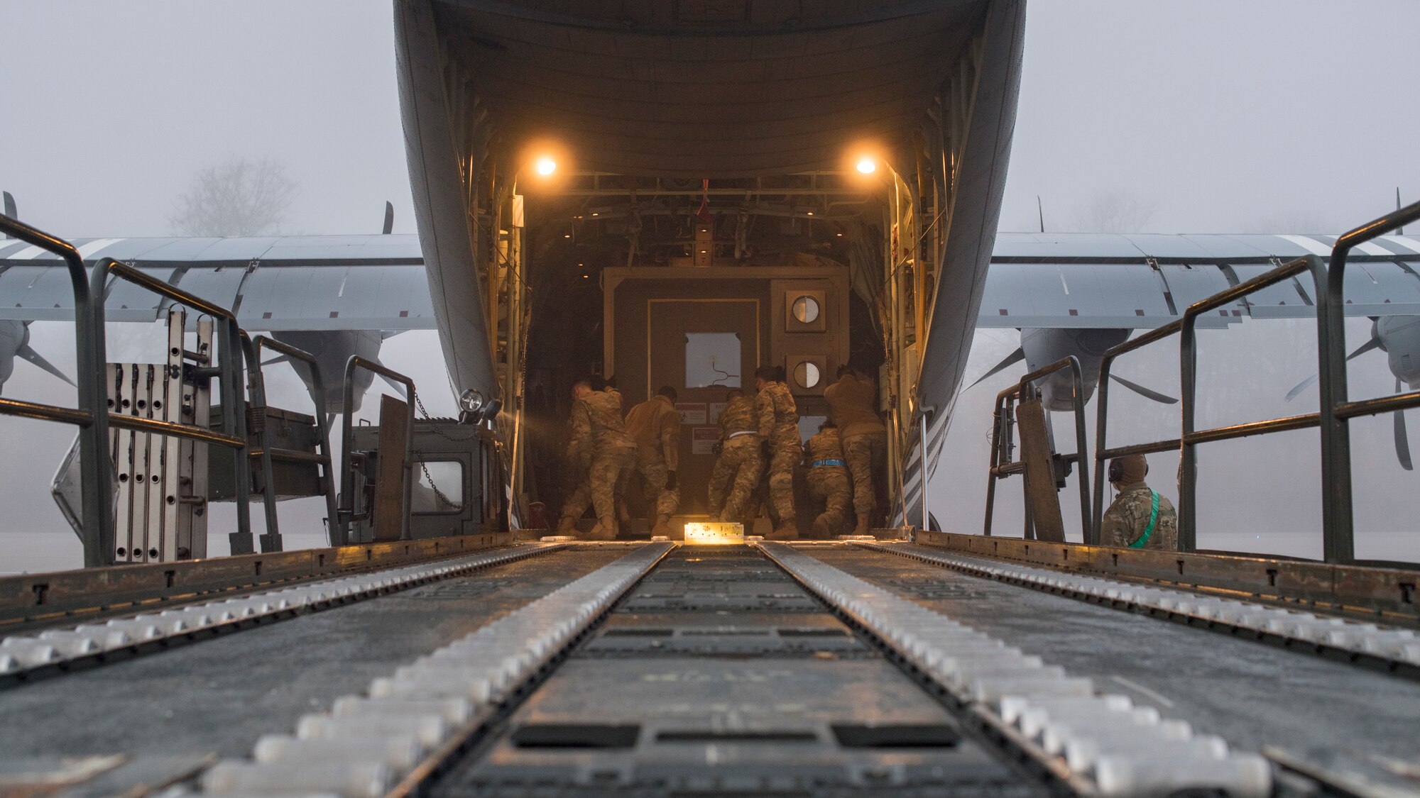 Airmen pushing an isolated containment chamber onto a plane.