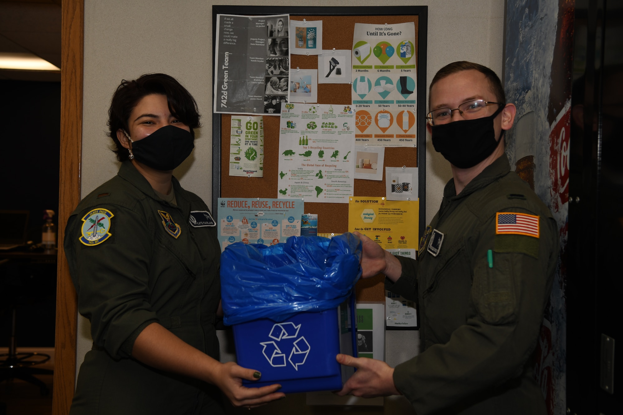 Two Airmen hold a recycling bin