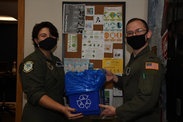 Two Airmen hold a recycling bin