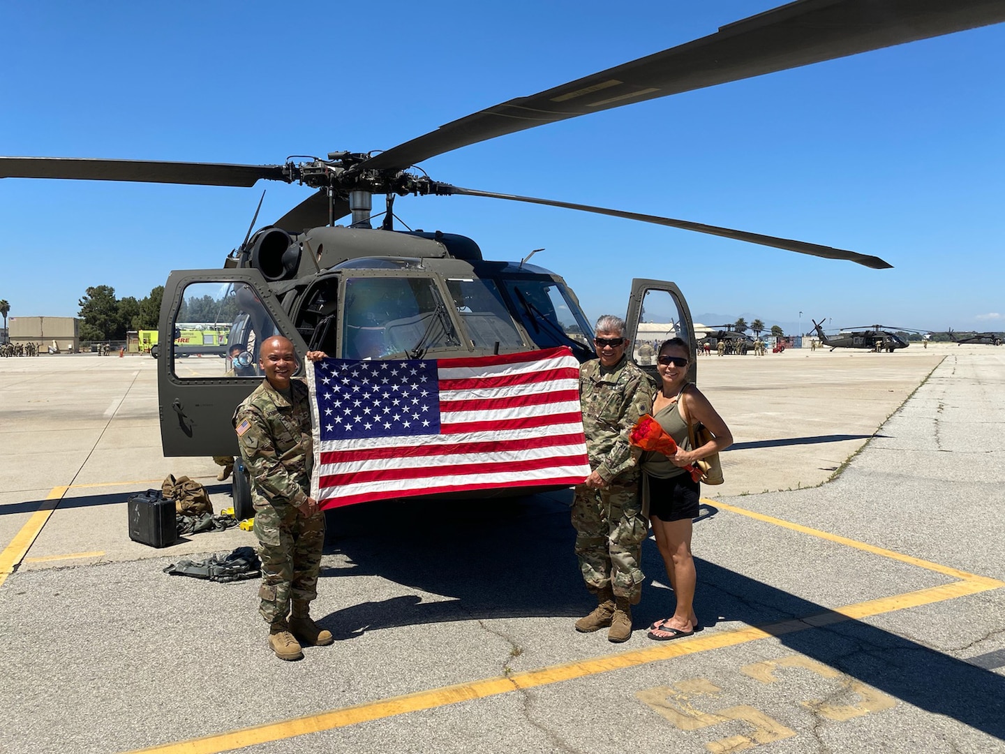 Three people stand in front of a helicopter holding an American flag