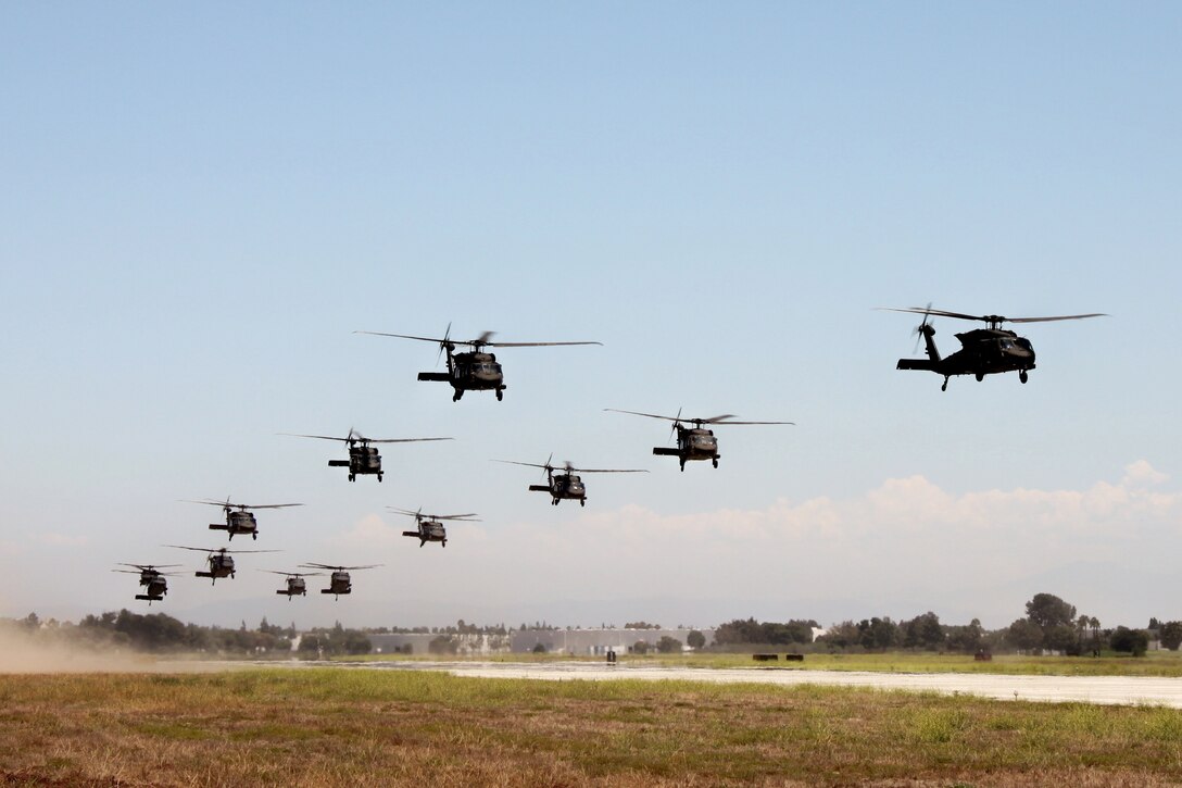 12 helicopters take off from an airfield in rapid succession.