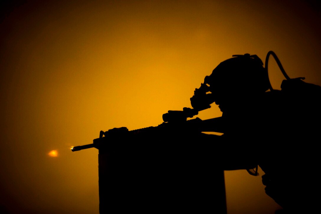 A Marine shown in silhouette fires a weapon.