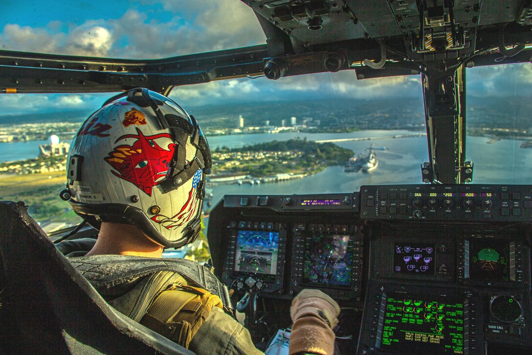 A Marine Corps pilot sits in a cockpit and looks out over a harbor.