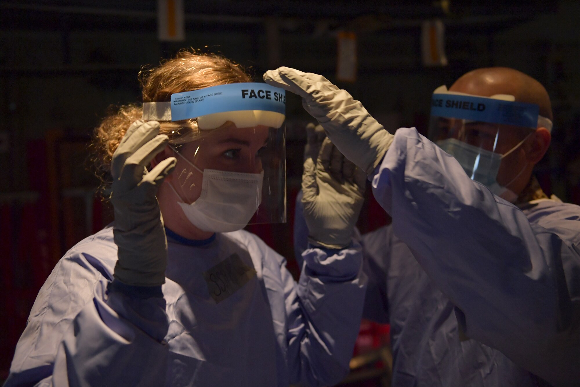 An Airman fixing the face shield on another Airman.